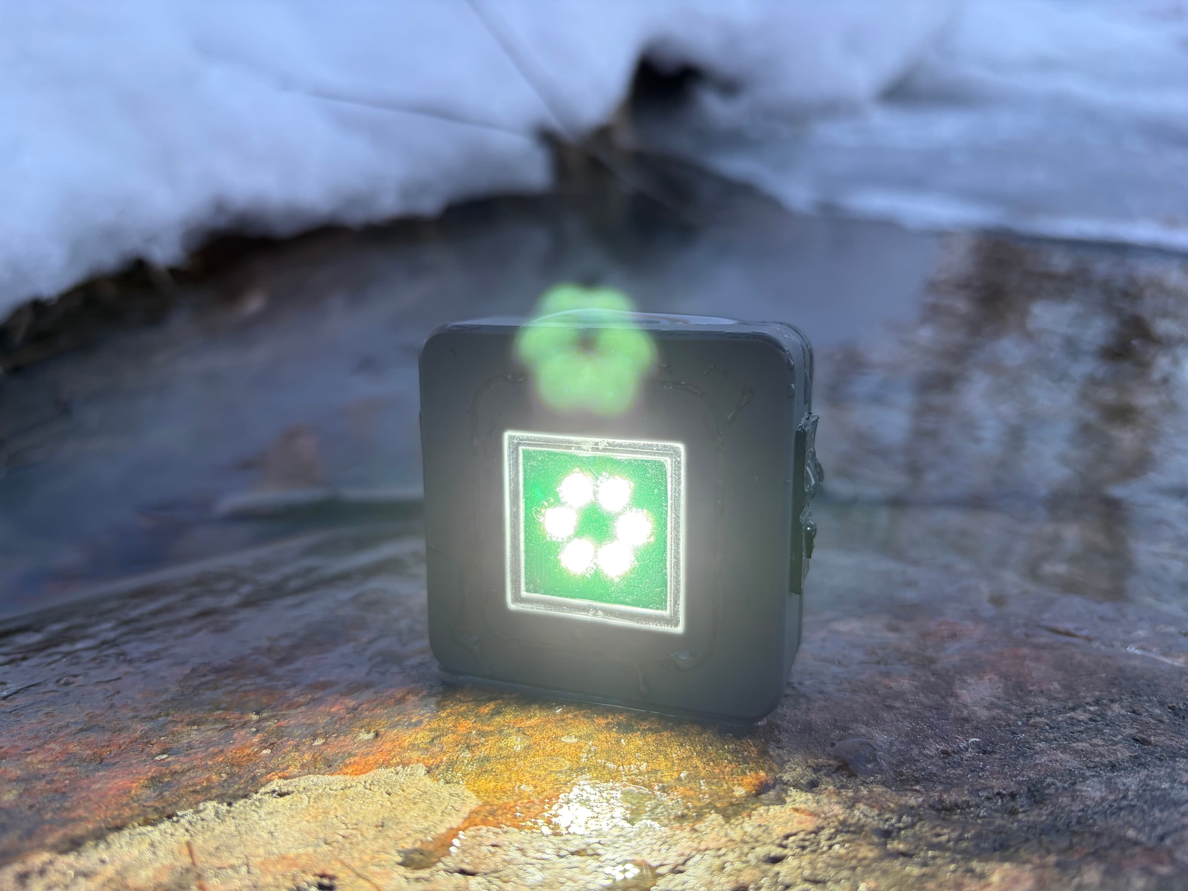Maglight M1 glowing on a rock beside a snow-edged stream